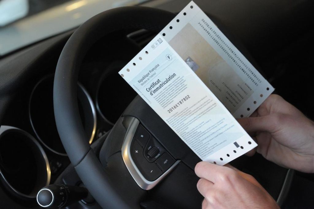 Mains tenant une carte grise et un smartphone